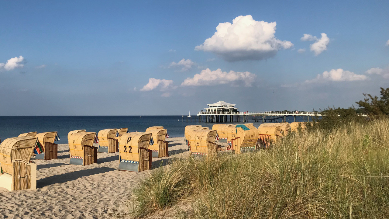 Blick von der Promenade in Timmendorfer Strand hinaus aufs Meer. Im Vordergrund stehen Strandkörbe. Im Hintergrund ist der Pavillon auf der Seebrücke zu sehen