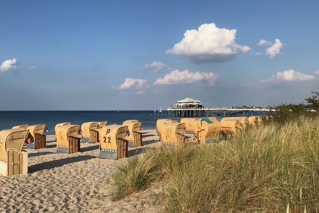 Blick von der Promenade in Timmendorfer Strand hinaus aufs Meer. Im Vordergrund stehen Strandkörbe. Im Hintergrund ist der Pavillon auf der Seebrücke zu sehen.