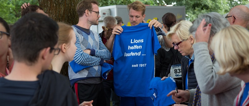 Eine Lions-Gruppe bereitet sich für den Spendenlauf vor. Auf den blauen T-Shirts steht mehrdeutig: Lions helfen laufend … seit 1917.