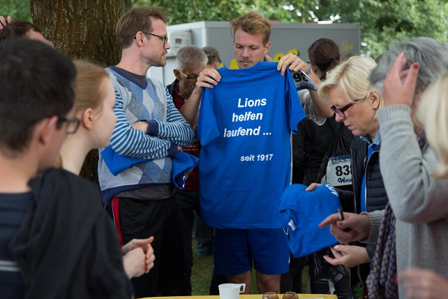 Eine Lions-Gruppe bereitet sich für den Spendenlauf vor. Auf den blauen T-Shirts steht mehrdeutig: Lions helfen laufend … seit 1917.