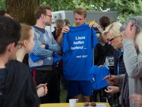 Eine Lions-Gruppe bereitet sich für einen Spendenlauf vor. Auf den blauen T-Shirts steht mehrdeutig: Lions helfen laufend … seit 1917.