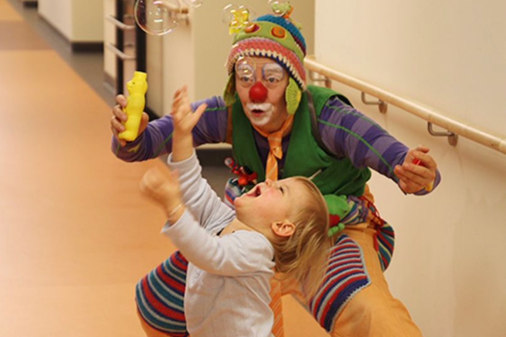 Klinikclown Upps spielt mit einem kleinen Kind auf dem Flur eines Krankenhauses