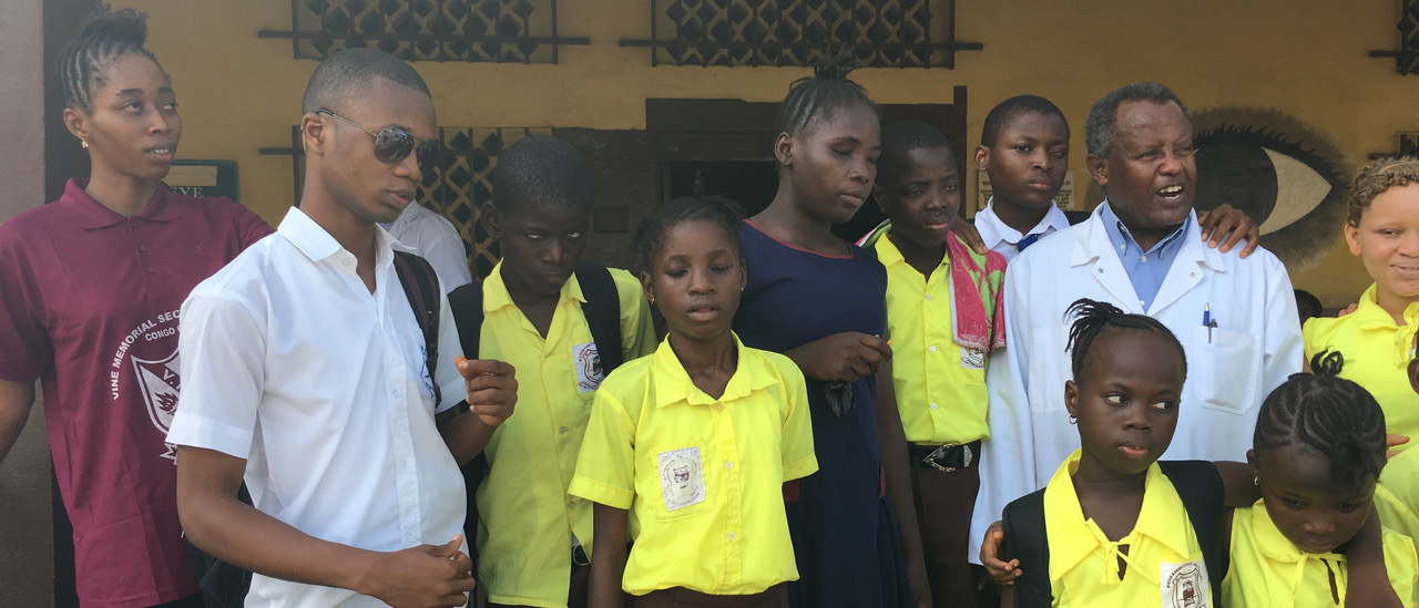 Sehbeeinträchtigte und blinde Kinder und Jugendliche stehen mit dem behandelnden Arzt vor der Augenklinik in Freetown Sierra Leone