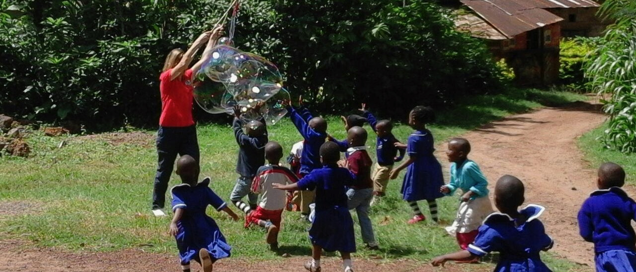 Kindergartenkinder laufen zur Betreuerin, die riesige Seifenblasen entstehen lässt