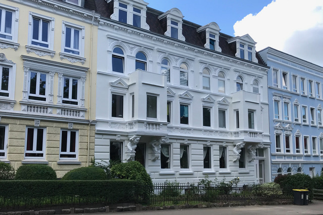 Straßenzug mit Mehrfamilienhäusern mit verschiedenfarbigen Jugendstil-Fassaden in hellgelb, weiß und hellblau