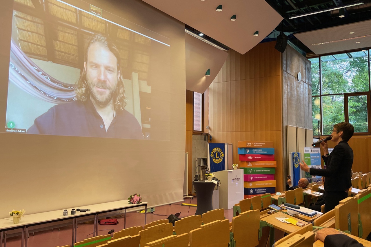 DG Annette Brand begrüßt den auf der Video-Leinwand zugeschalteten Benjamin Adrion