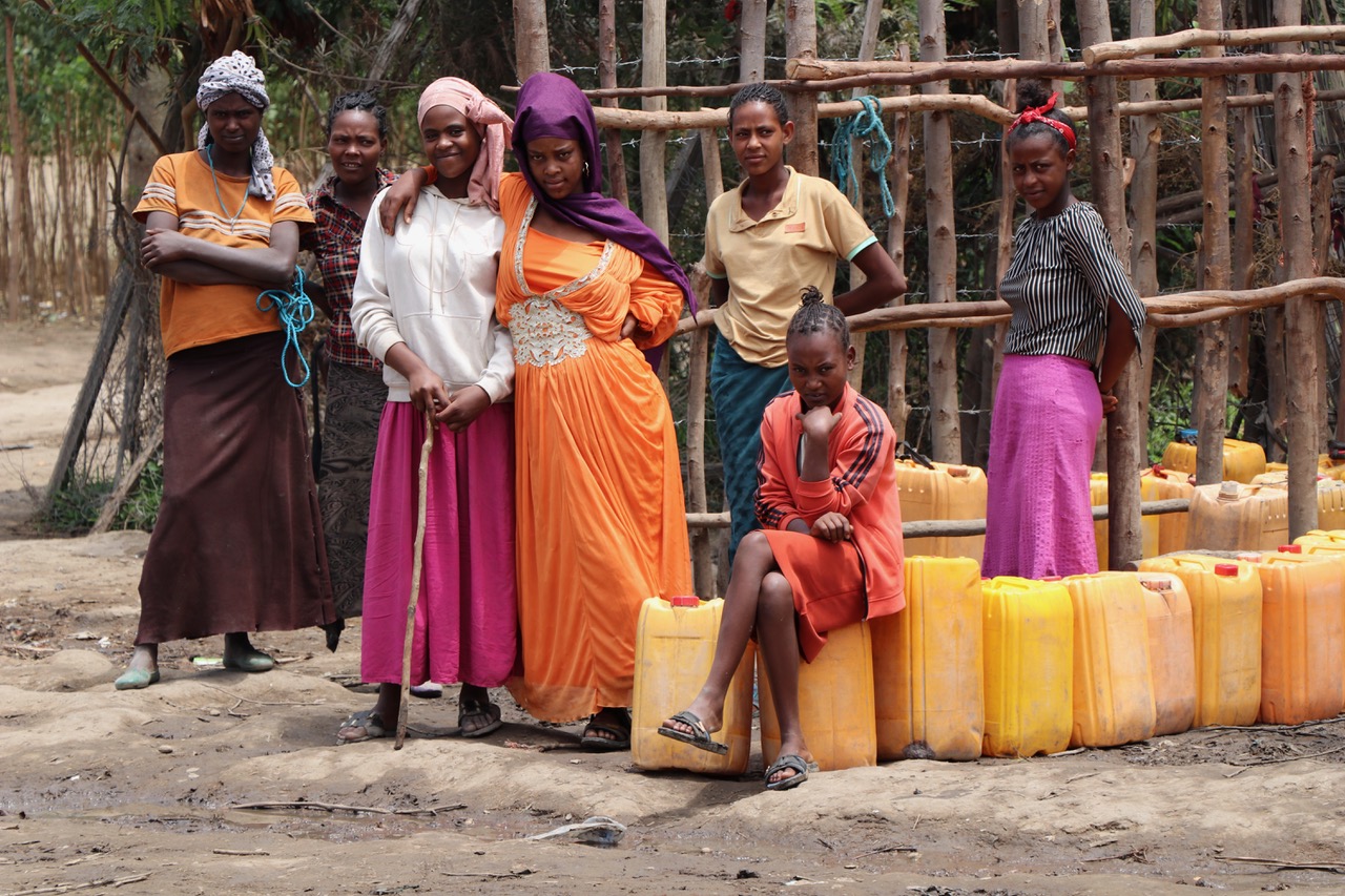 Mehrere Frauen warten mit großen gelben Kanistern aus der Wasserausgabestelle