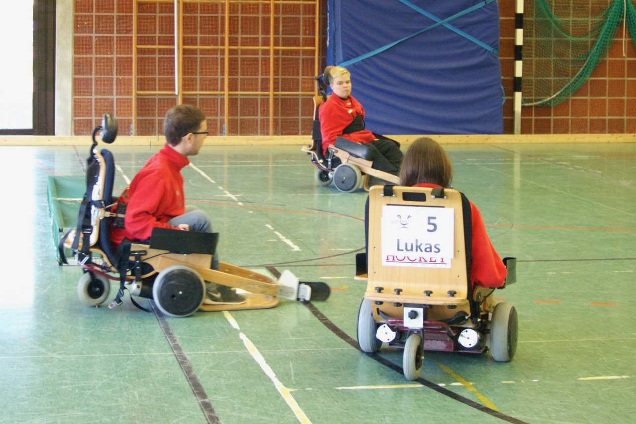 Drei Jungs spielen mit ihren Elektrorollstühlen Hockey