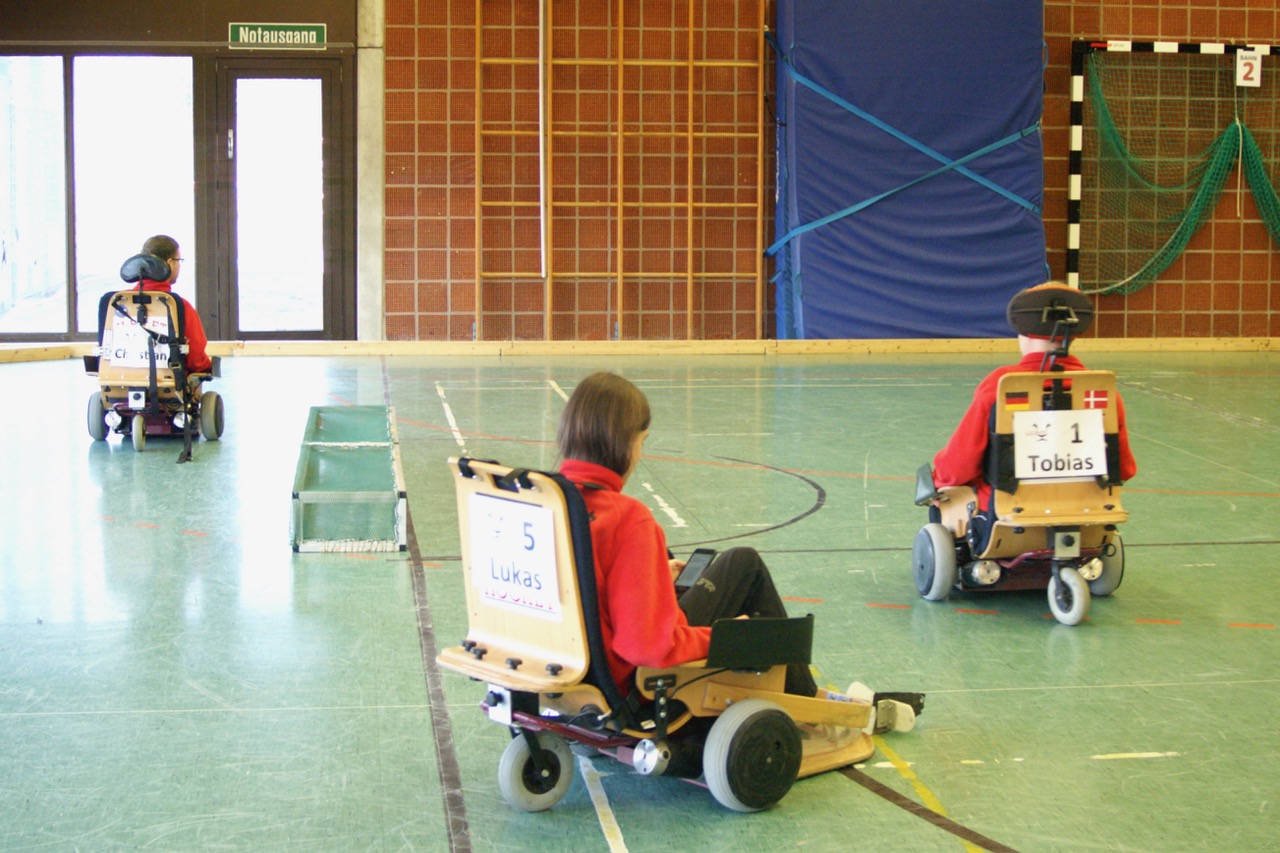 Drei Jungs spielen mit ihren Elektrorollstühlen Hockey