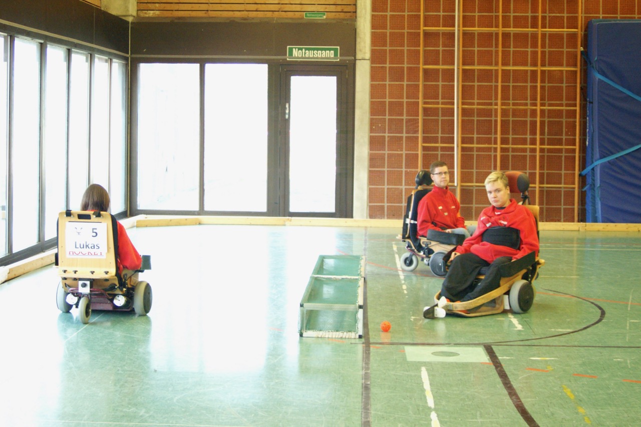 Drei Jungs spielen mit ihren Elektrorollstühlen Hockey